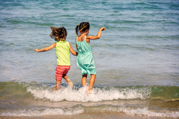 Activity on the beach in summer. A happy little girl and a little boy jump into the sea on a sunny...