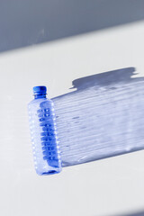 Blue plastic water bottles on white blue background with sunlight shadow and sun flare, Minimal top...