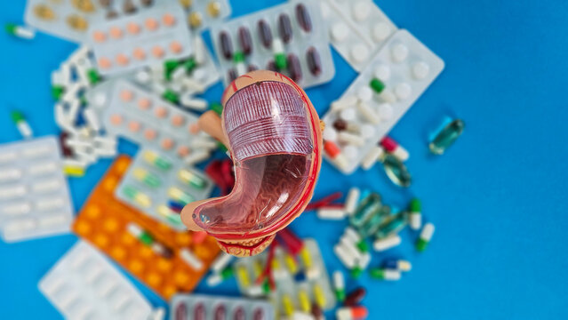 Colorful stomach model surrounded by various medicines and capsules on blue background