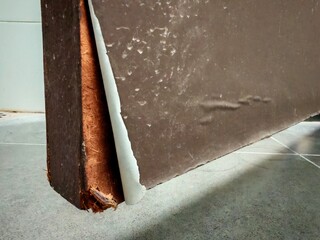 A close-up view of the bottom edge of a door showing peeling laminate and exposed fiberboard due to...