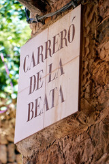 Street sign with bold serif letters on ceramic tiles mounted to a rustic stone wall, surrounded by...