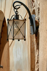 Vintage black metal wall lantern with clear glass panels, mounted on textured beige wall in...