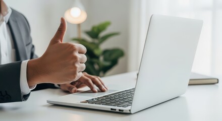 A businessman gives a thumbs up while working on a laptop