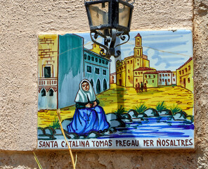 Hand-painted ceramic tile mural shows woman in folk dress by stream, with historic village...