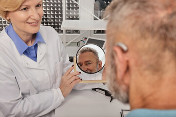 Hearing aids and solutions. Audiologist offers BTE hearing aids to man patient with hearing...