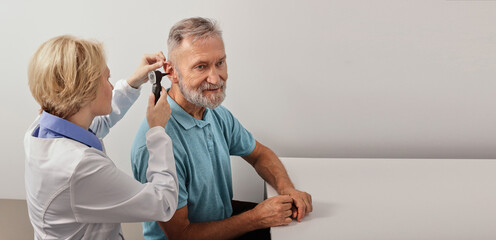 Elderly man while ear test with audiologist with otoscope at medical office, close-up. Diagnosis of...