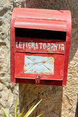 Red vintage mailbox with peeling paint and white text hangs on a rustic stone wall in sunlight, evoking nostalgic charm. Red mailbox; vintage wall;