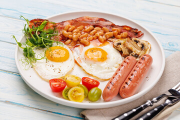 A classic breakfast plate featuring sunny-side-up eggs, crispy bacon, sausages, and fresh tomatoes