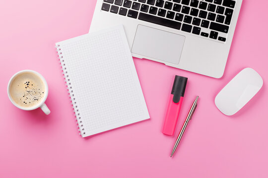 Top view of a pink desk with office supplies, coffee cup, and blank notepad