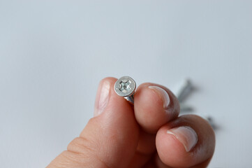 close-up of a person holding a small metal screw, concept of home improvement, hardware details,...