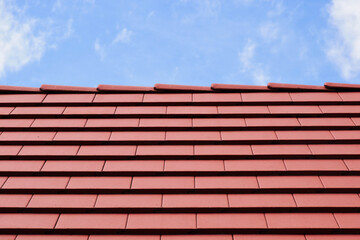 sloped red clay roof and ridge detail. new bright brown clay house roof tiles. closeup view. construction industry and building materials concept. clear blue sky with white clouds. bright sunlight.