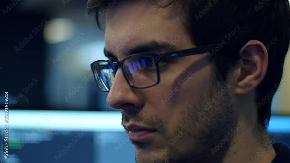 Poster focused young man with glasses working at computer in dark environment illuminated by screen light r