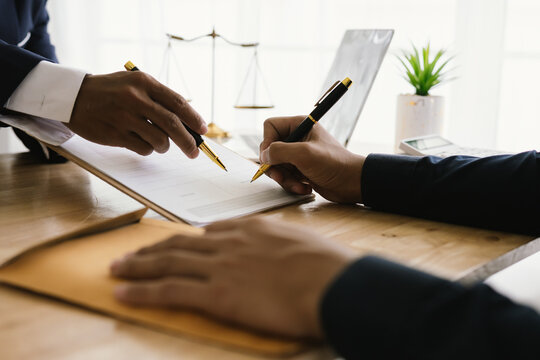 Close-up of lawyer giving legal advice showing gavel, scales and expert examining documents, representing law, justice, court process, agreements and ethical decisions in a formal setting.