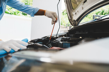 Mechanic wearing gloves inspecting car engine, checking engine oil with dipstick, focusing on...