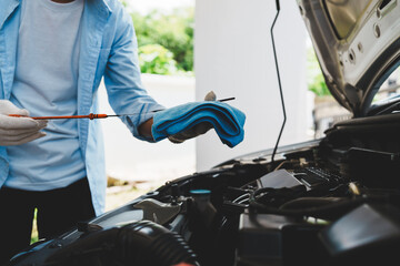 Mechanic wearing gloves inspecting car engine, checking engine oil with dipstick, focusing on...