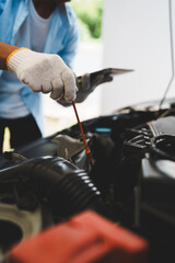 Mechanic wearing gloves inspecting car engine, checking engine oil with dipstick, focusing on maintenance and repair to ensure car performance, safety and efficient car care in the repair shop.