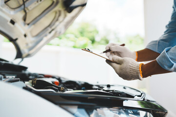 A mechanic wearing gloves inspects a car engine and keeps a checklist, focusing on maintenance and...