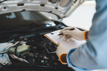 A mechanic wearing gloves inspects a car engine and keeps a checklist, focusing on maintenance and...