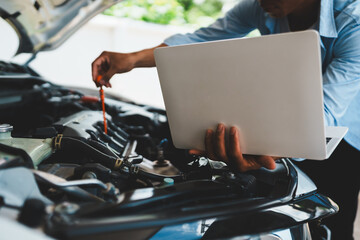 Mechanic checking engine oil using laptop to thoroughly inspect engine Focuses on maintenance and...