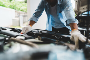 A professional mechanic wearing gloves uses wrenches to repair a car engine under the open hood,...