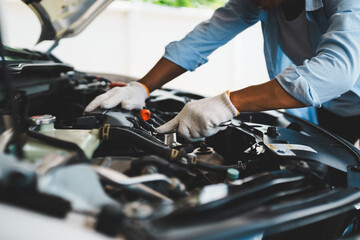 A professional mechanic wearing gloves uses wrenches to repair a car engine under the open hood,...
