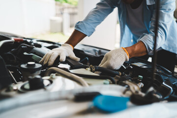 A professional mechanic wearing gloves uses wrenches to repair a car engine under the open hood,...