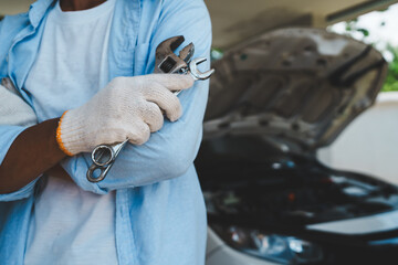 A professional mechanic wearing gloves uses wrenches to repair a car engine under the open hood,...
