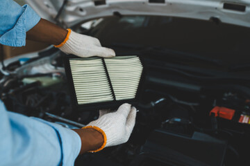 A gloved mechanic inspects and changes a car's air filter under an open hood, performing essential...