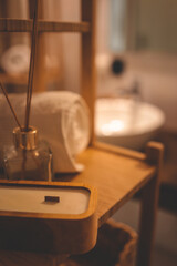 Close-up of a wooden candle, glass aroma diffuser, and rolled towel on a bamboo shelf in a cozy bathroom. Soft light and natural textures create a relaxing atmosphere