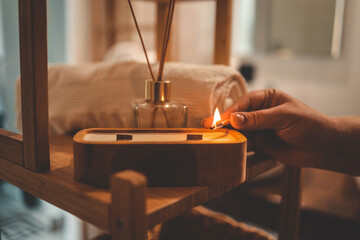 A cozy bathroom moment as a person lights a handmade wooden candle with two wicks, surrounded by a...