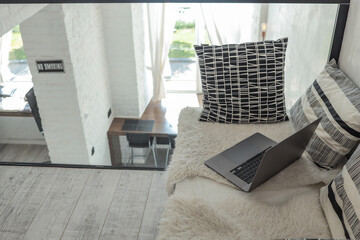 Cozy loft nook with soft pillows, fluffy blanket, and open laptop overlooking bright modern...