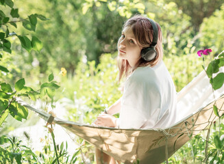 Teenager relaxing in hammock listening to music with headphones in lush green garden