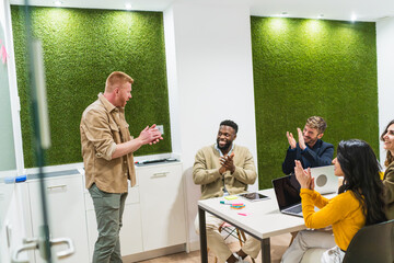 Diverse team of young professionals clapping after a successful presentation in a modern coworking...