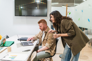 Business colleagues working together, analyzing data on a laptop in a bright, modern coworking...