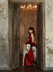 Young woman with high hairstyle in red art deco dress with boa and two dogs in room with chandelier...