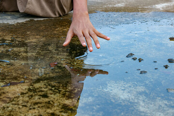 Hand Touching Water Surface in a Puddle Creating Ripples