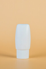 Plastic white tube for cream or lotion. Skin care or sunscreen cosmetic with stylish props on cream background.