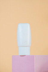 Plastic white tube for cream or lotion. Skin care or sunscreen cosmetic with stylish props on cream background.
