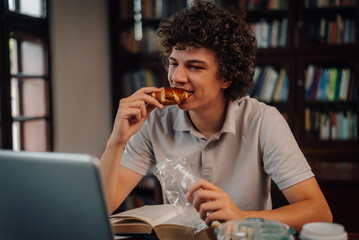 Young student eating pastry while studying at home library