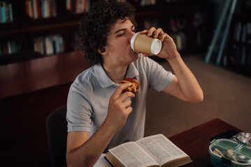 Student drinking coffee and eating pastry while studying in library