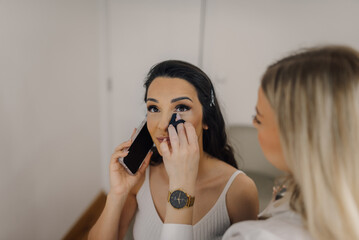 Makeup artist applying makeup on model using phone during session