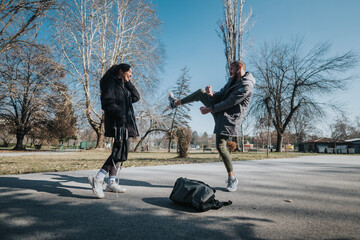 Two teenagers enjoy a sunny day in a park, engaging in playful interaction surrounded by bare...