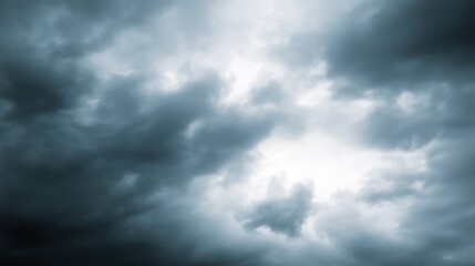 Obraz premium Dramatic dark storm clouds swirling in the sky, creating a moody atmosphere with varying shades of gray and hints of light breaking through the dense cloud cover