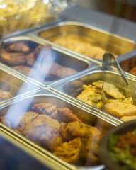 Assorted traditional Indonesian fried snacks such as bakwan, fried tofu, and tempeh served in a food warmer inside a local restaurant or warung.