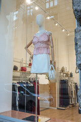 Mannequin in a pink ruffled blouse and white skirt holding a cream handbag, displayed in a boutique...