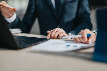 Business people collaborating and discussing financial documents during meeting. Hands shown...