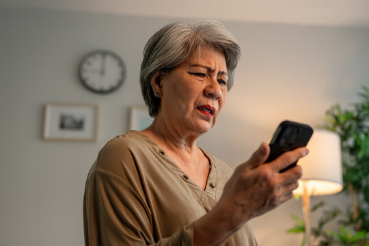 Depressed Asian senior woman sit alone on bed and looking at smartphone. 