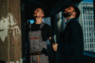 Interior construction site with two professionals inspecting details. One man wears work overalls,...