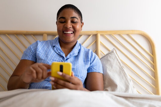 Happy woman using smartphone in bed in the morning