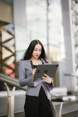 Confident businesswoman standing outdoors in the city holding a tablet, showing modern style,...